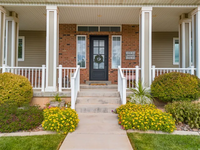 Brick facade with a covered porch, concrete steps, white railings, and mature landscaping