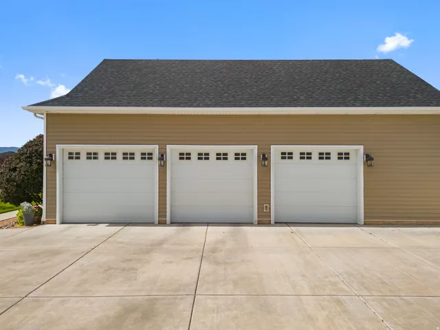 Three-car garage with white paneled doors, decorative windows, and exterior wall sconces