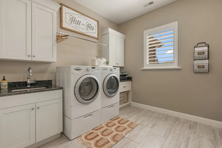 Laundry area with white cabinetry, granite countertop, undermount sink, and wood-finish tile flooring