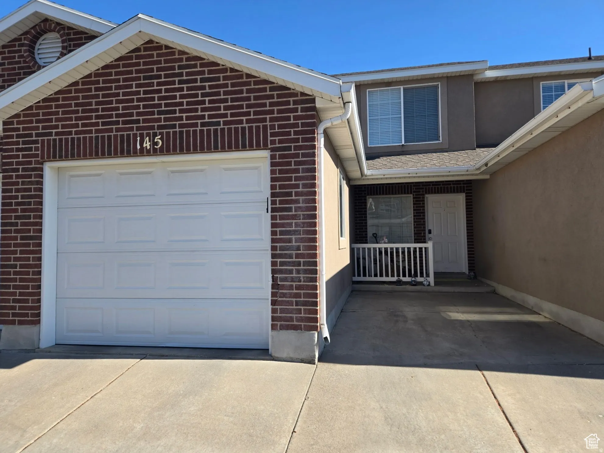 Brick and stucco exterior with an attached garage, covered entryway, white front door, and upper-level windows