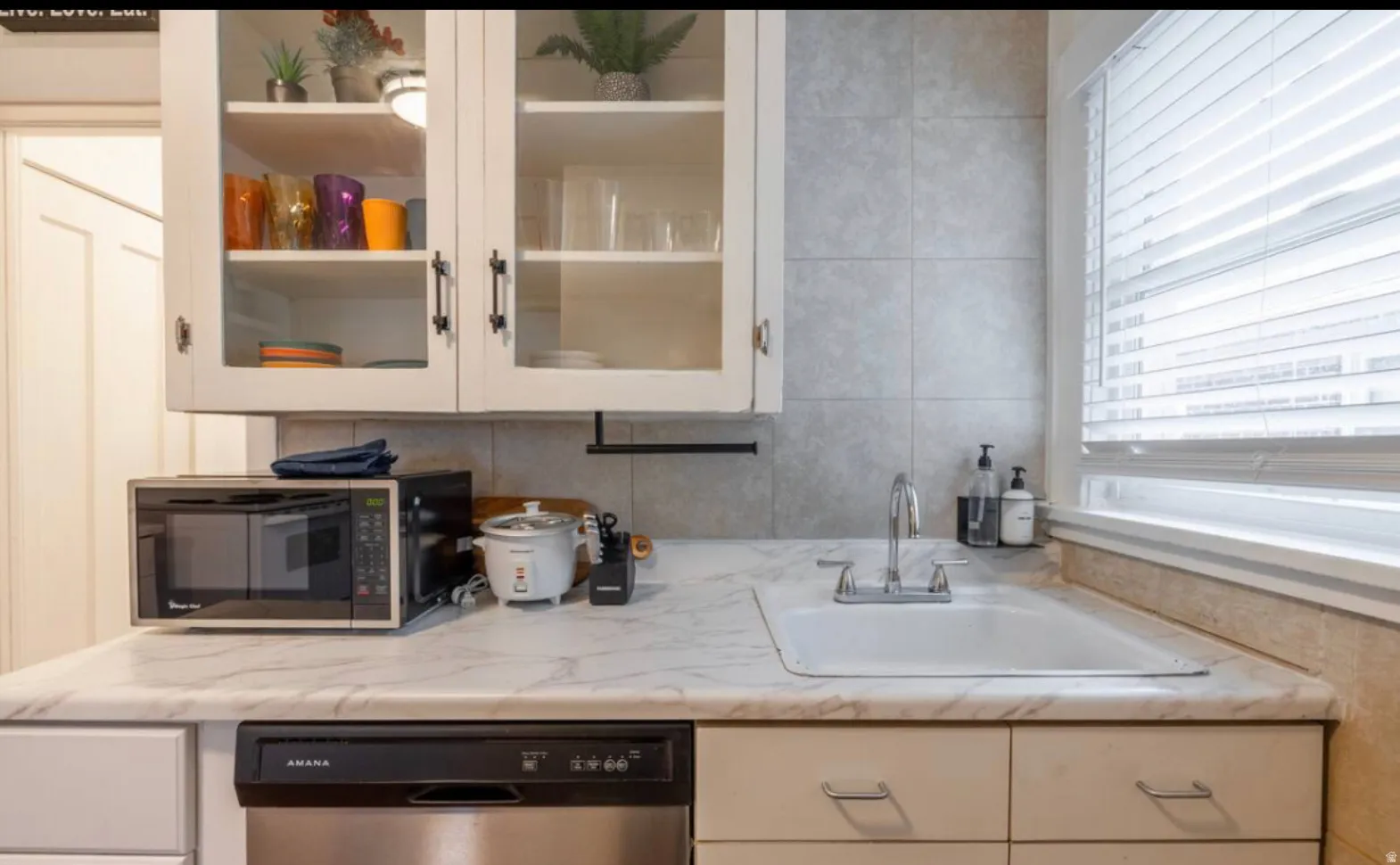 White cabinetry with glass inserts, laminate countertops, tile backsplash, built-in dishwasher, and an undermount sink