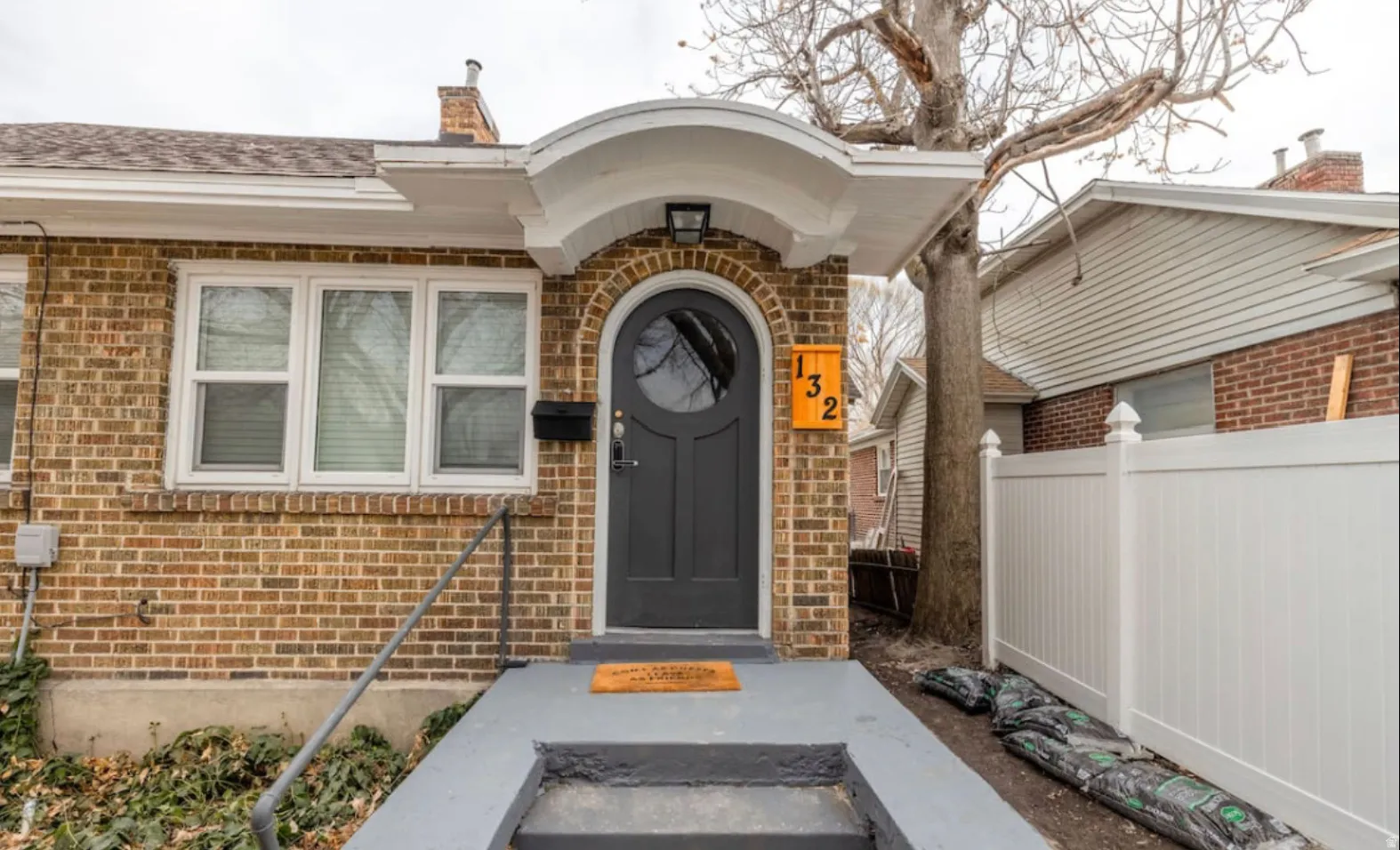 Brick exterior with white trim, arched entryway, dark gray front door, and a white privacy fence