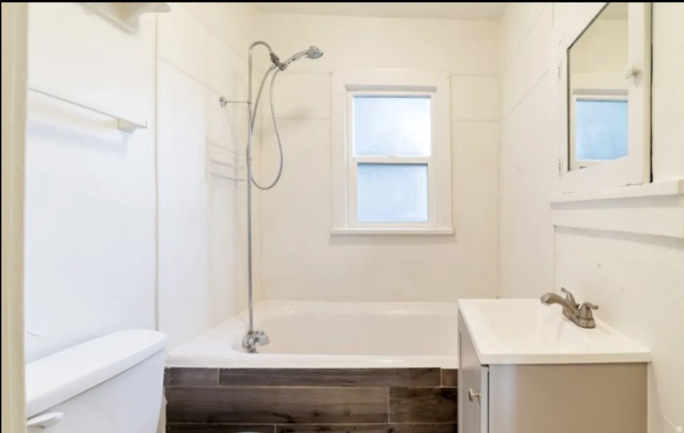 Built-in bathtub with a wall-mounted showerhead, single window with privacy glass, vanity with an integrated sink, and wood-finish tile flooring