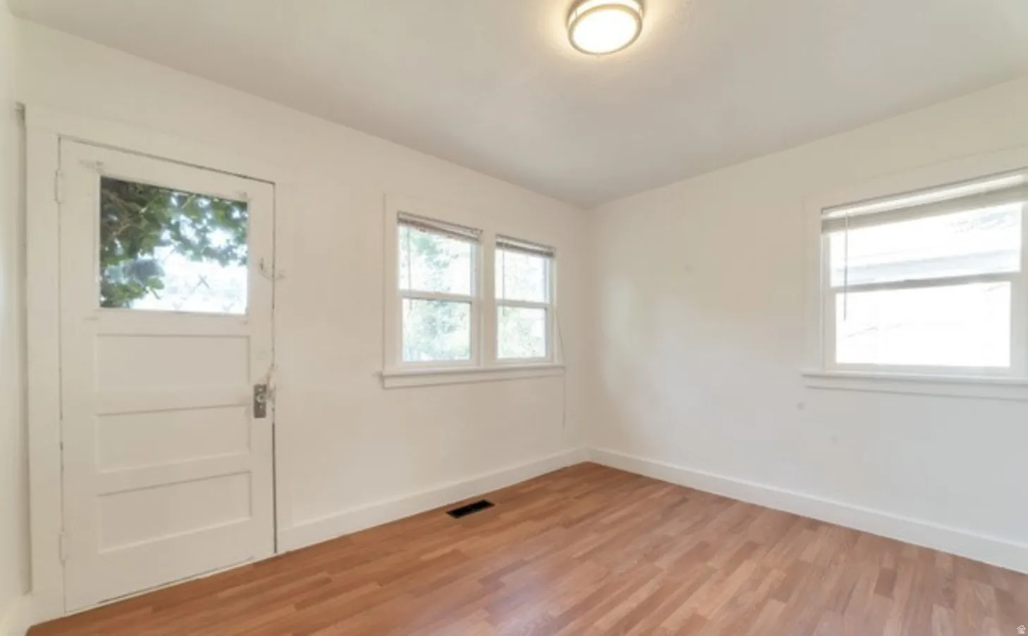 Hardwood flooring, multiple windows, overhead lighting, white walls, and a glass-paneled door