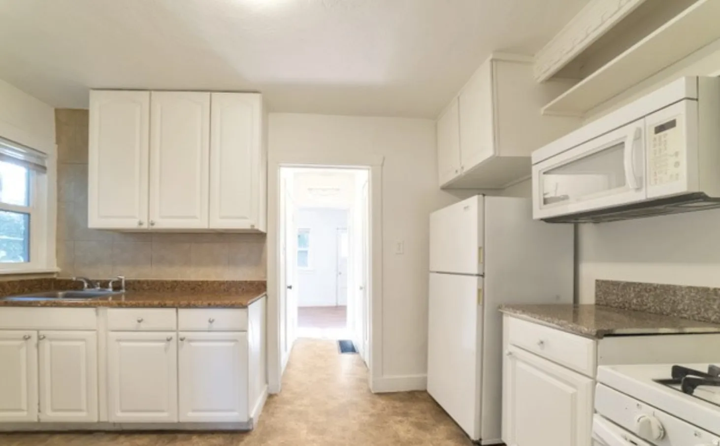 White cabinetry, stone-finish countertops, tiled backsplash, and built-in microwave