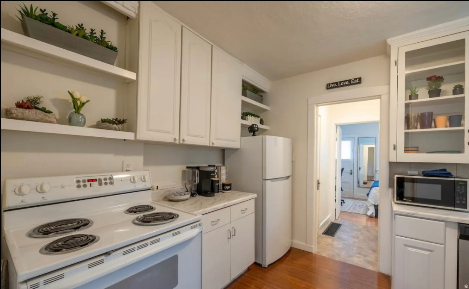 White cabinetry, open shelving, white appliances, and wood-finish flooring