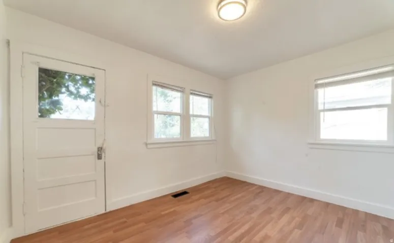 Hardwood flooring, multiple windows, overhead lighting, white walls, and a glass-paneled door