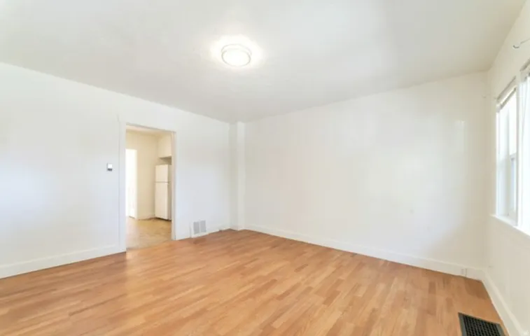 Hardwood-style flooring, white painted walls, ceiling-mounted light fixture, window with natural light, and a doorway opening