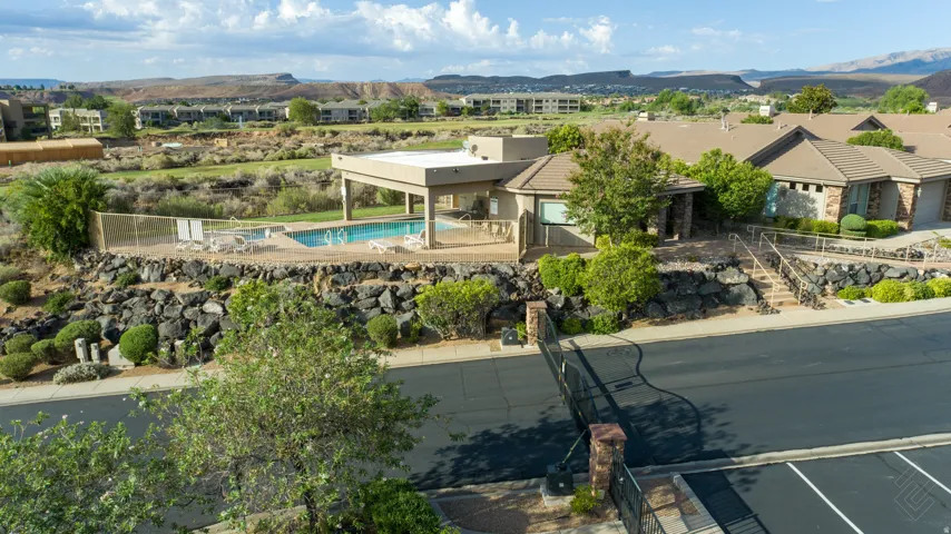 Community pool with covered patio, adjacent to landscaped rock retaining walls and mature shrubbery