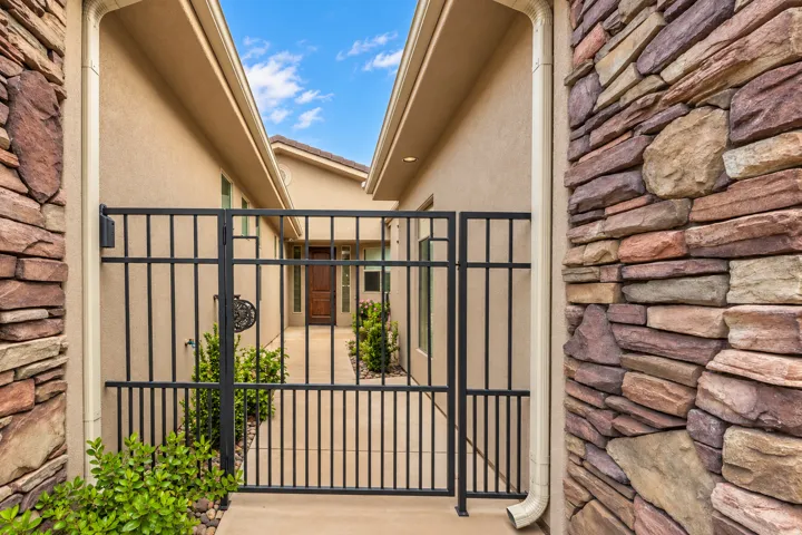 Gated entry with wrought iron accents, stone facade, stucco exterior, and concrete pathway