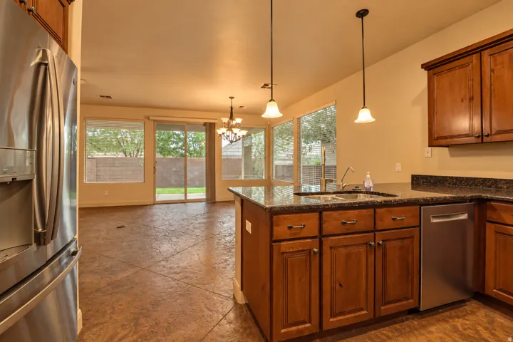 Kitchen island with an undermount sink and granite countertops, stainless steel appliances, wood-finish cabinetry, and pendant lighting