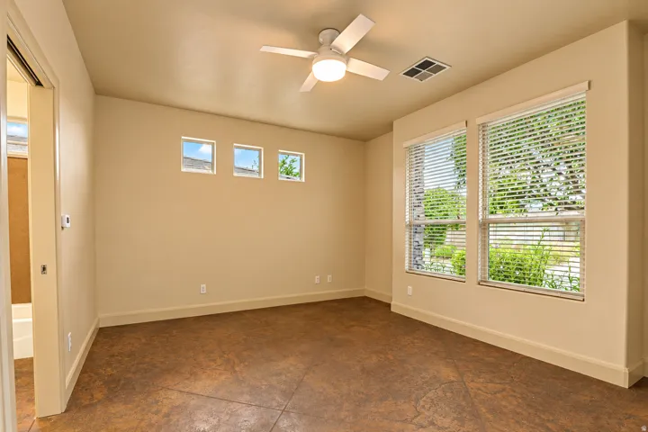 Spacious room featuring rich, textured floor, multiple windows with blinds, three high transom windows, and a ceiling fan with integrated lighting