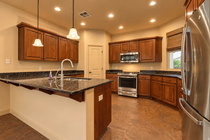 Kitchen featuring wood cabinetry, stainless steel appliances, dark stone countertops, and a center island with a built-in sink