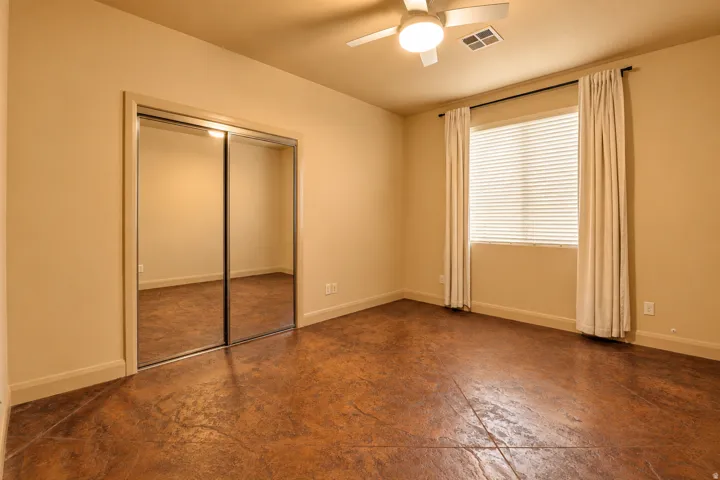 Textured flooring, ceiling fan with integrated lighting, window with blinds, and mirrored closet doors