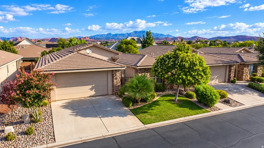 Exterior featuring a tiled roof, stone accents, mature landscaping, and an attached garage with a concrete driveway