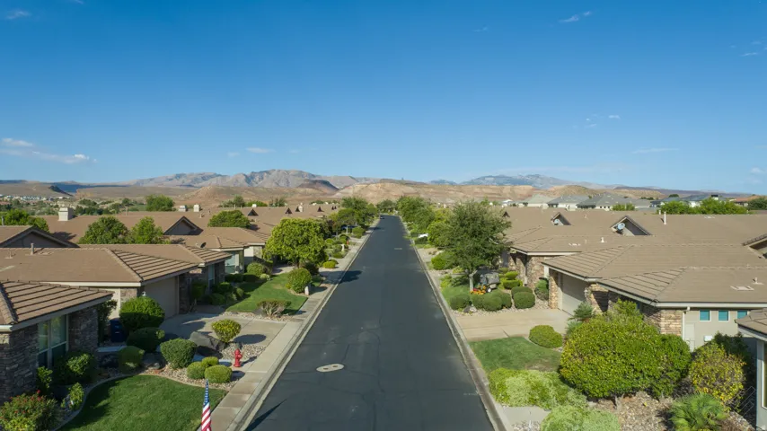 Residential street with uniform tiled roofs and manicured landscaping, framed by distant mountains