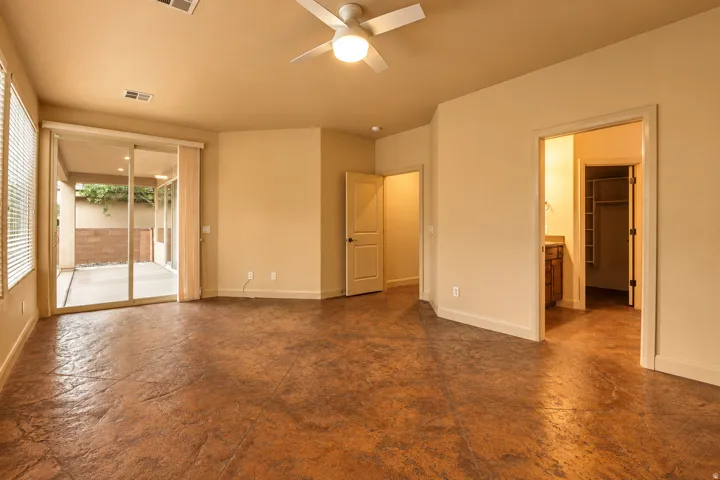 Stained concrete flooring, ceiling fan with integrated lighting, sliding glass door to exterior patio, recessed lighting, and built-in closet shelving