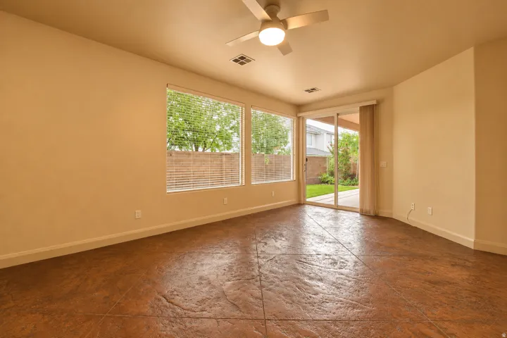 Textured flooring, ceiling fan with integrated lighting, multiple windows with horizontal blinds, sliding glass door, and a private patio