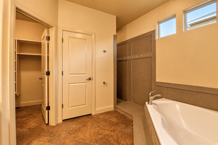 Soaking tub with brushed nickel fixtures, walk-in shower with textured wall panels, high transom windows, and built-in closet shelving