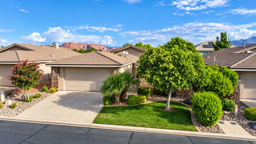 Paved driveway, attached garage, stone accents, tiled roof, and landscaped front yard with mature trees
