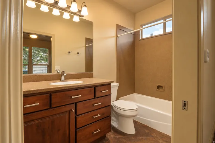 Wood-finish vanity with an integrated sink and brushed nickel faucet, large vanity mirror, built-in bathtub with a wall-mounted shower, and a high-set window