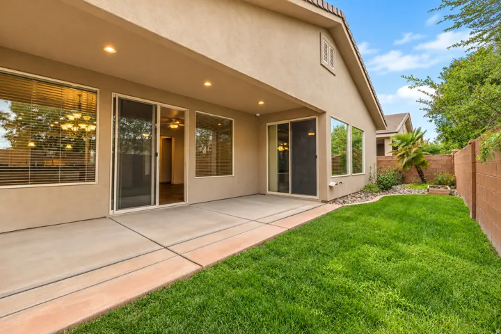 Covered concrete patio with recessed lighting, multiple sliding glass doors, a manicured lawn, and perimeter fencing