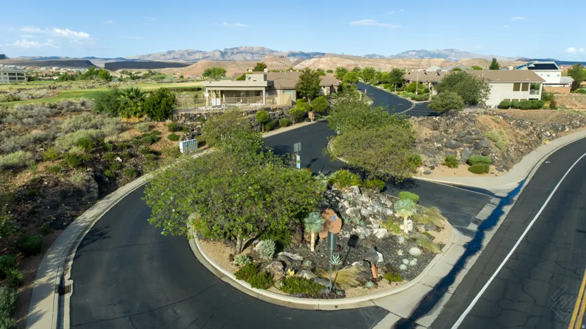 Paved roads with curbs, desert landscaping, surrounding residential structures, distant mountainous terrain, and a golf course