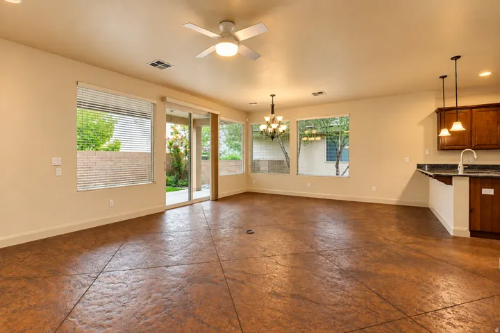 Expansive room featuring textured flooring, multiple windows, a sliding glass door, a ceiling fan with integrated lighting, and a kitchen peninsula with cabinetry and pendant lighting
