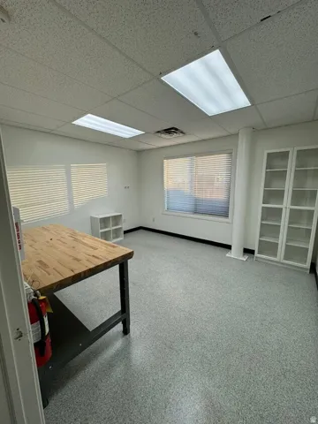 Unit D Recessed lighting, drop ceiling, multiple windows with blinds, built-in shelving, and speckled flooring