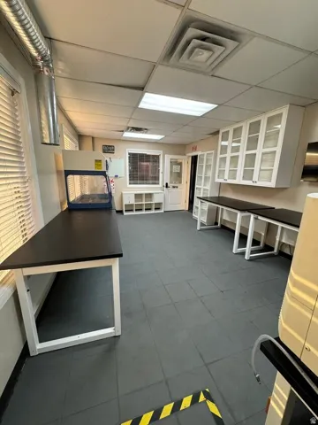 Spacious work area featuring multiple fixed workstations, overhead cabinetry with glass doors, and durable tile flooring