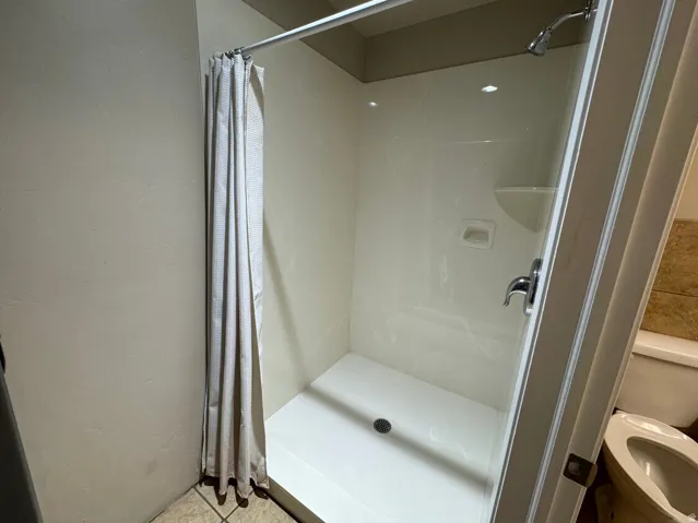 Enclosed shower stall with a white acrylic base and walls, featuring a chrome shower head and fixtures