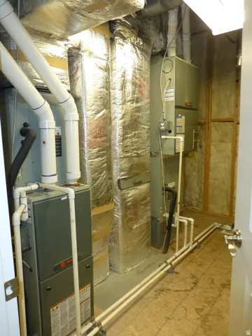 Dual-system mechanical room featuring two furnaces, insulated ductwork, and exposed piping