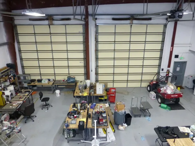 Unit D Industrial warehouse space featuring two large roll-up doors, high ceilings, polished concrete flooring, and suspended fluorescent lighting