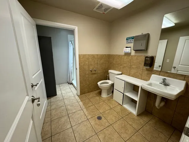 Tiled flooring, partial wall tile, wall-mounted sink, toilet, and an adjacent shower enclosure