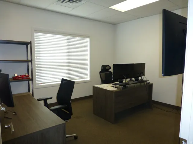 Unit D- Recessed lighting with suspended ceiling tiles, textured carpet flooring, and a window with horizontal blinds