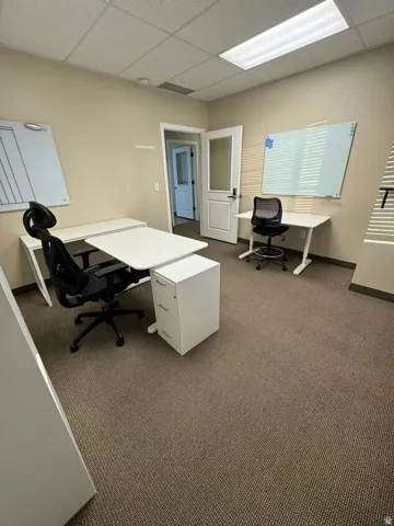 Unit D- Commercial-grade carpet flooring, drop ceiling with integrated fluorescent lighting, and a white paneled door with glass insert