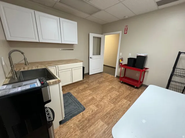 Wood-finish flooring, white cabinetry, stainless steel sink, pull-down faucet, and white door with frosted glass panel
