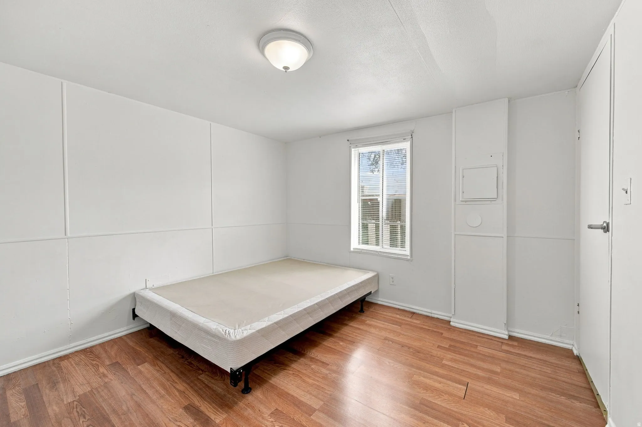 Wood-finish flooring, white paneled walls, and a single window with white trim