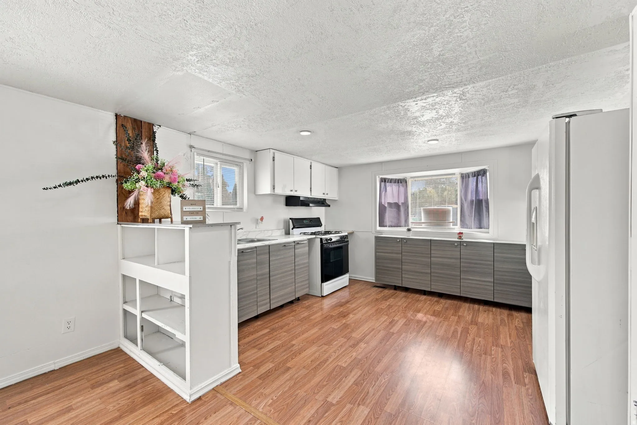 Kitchen featuring wood-finish flooring, white upper cabinetry, gray lower cabinetry, and a built-in shelving unit