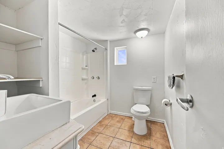White bathtub with shower, white toilet, tile flooring, and built-in shelving