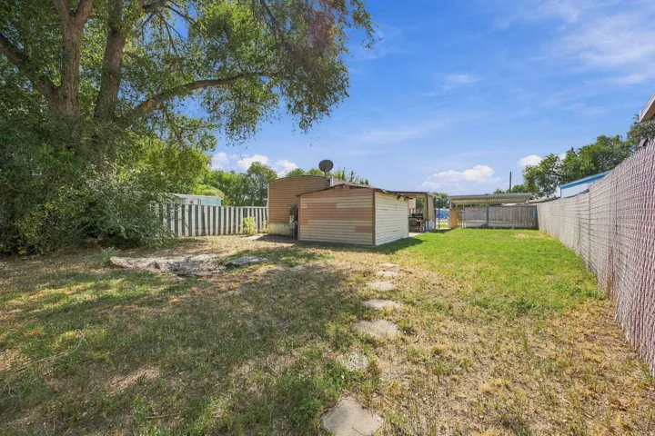 Expansive backyard featuring a partial grass lawn, mature trees, a storage shed, and a covered patio area