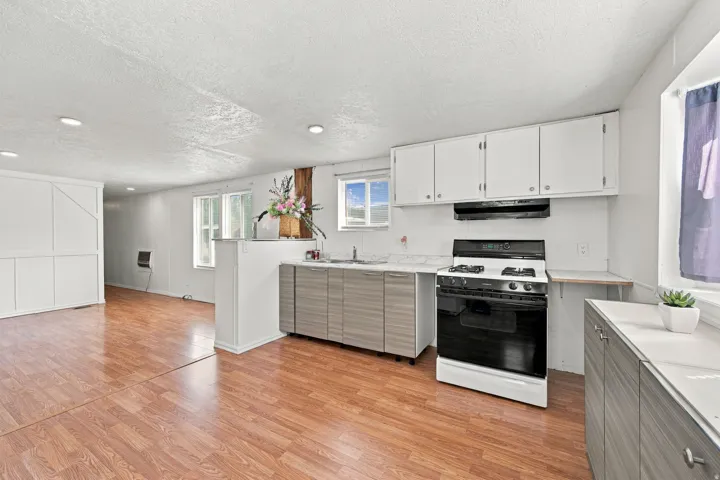 Kitchen featuring white upper cabinetry, wood-finish flooring, a gas range, and a dual-basin sink with a gooseneck faucet