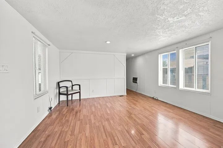 Wood-finish flooring throughout, multiple windows with blinds, recessed ceiling lighting, and a white paneled wall accent