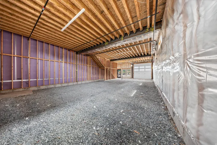 Unfinished interior space featuring exposed wood joists and subflooring, partial wall framing with insulation, a gravel floor, and a white paneled garage door