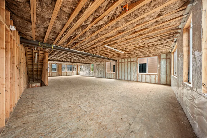 Spacious unfinished interior with exposed wood framing, multiple windows, and a partially insulated ceiling