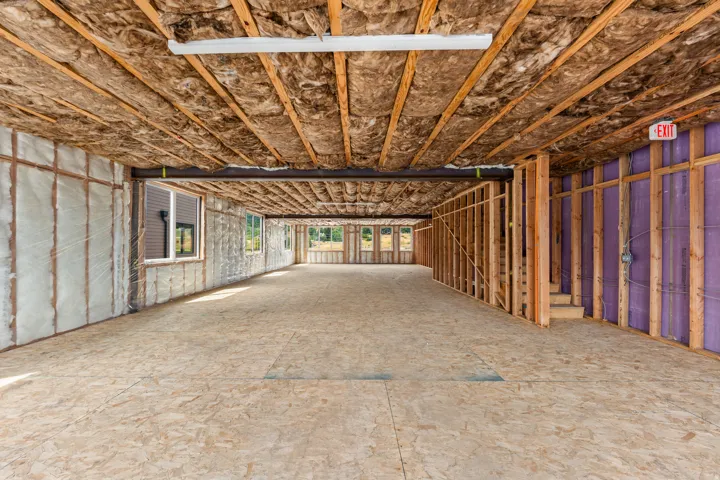 Expansive unfinished space featuring exposed ceiling joists, wood-finish subflooring, multiple windows, and a partially framed wall with purple insulation