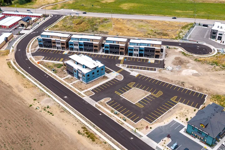 New construction multi-story buildings with contemporary facades, paved roadways, dedicated parking areas, and surrounding undeveloped land