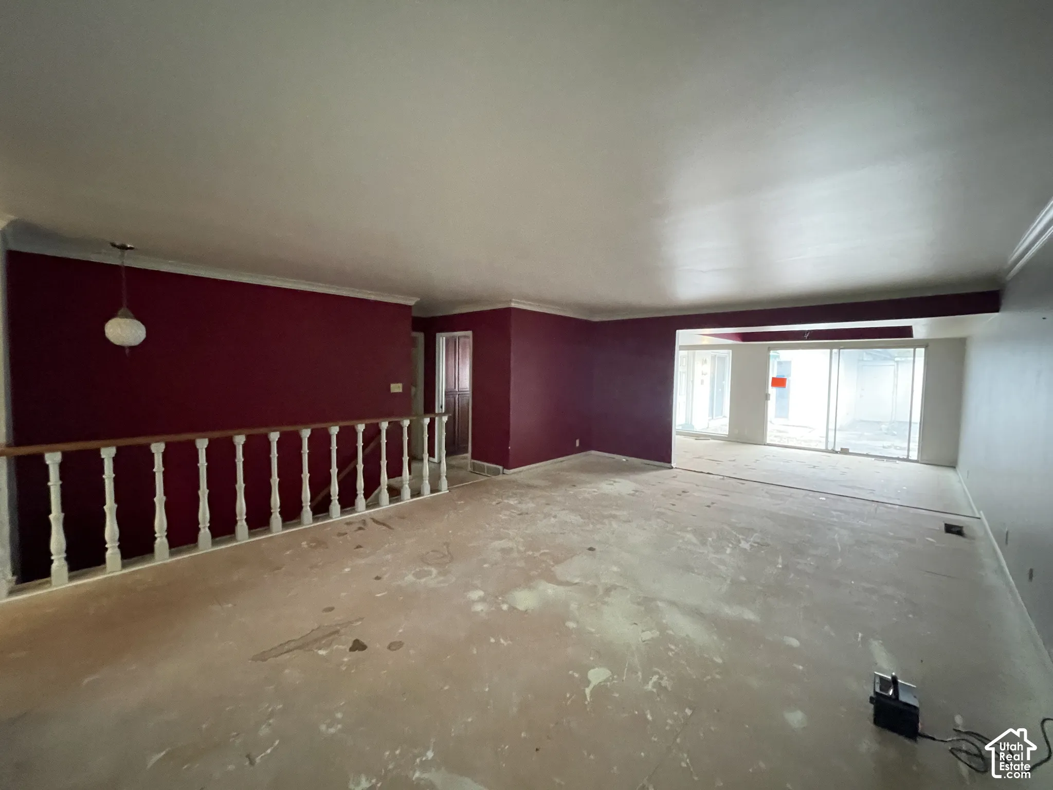 Open-concept area featuring white spindle railing, sliding glass doors, crown molding, and a neutral pendant light fixture