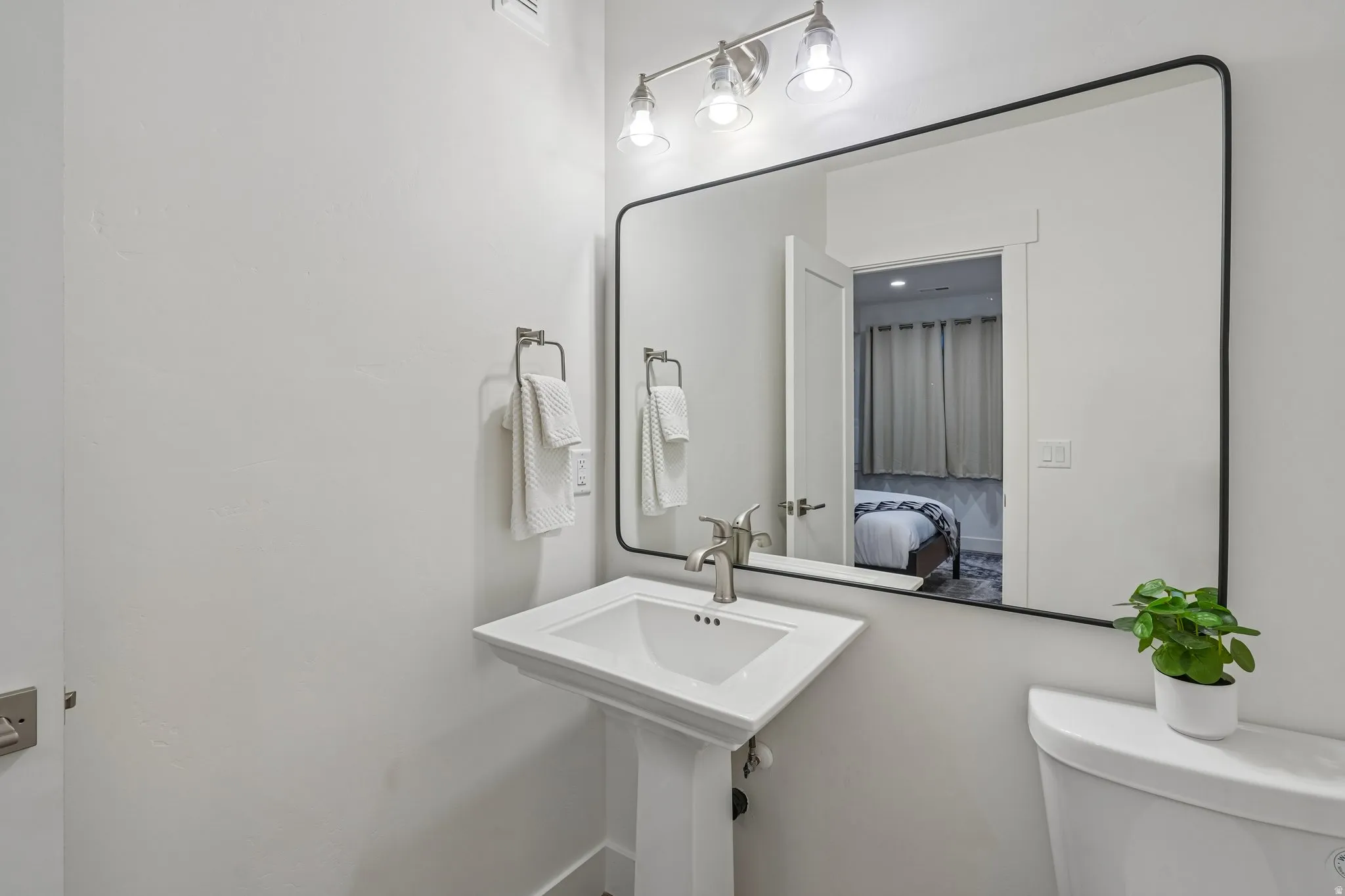 Pedestal sink with brushed nickel faucet, framed mirror, and wall-mounted vanity lighting