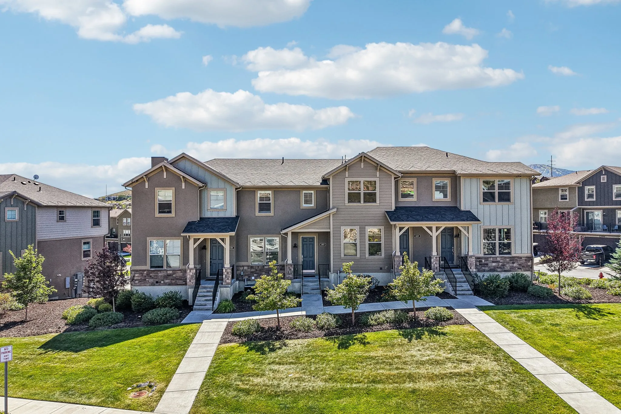 Townhome exterior featuring stone accents, covered entryways, and a manicured lawn